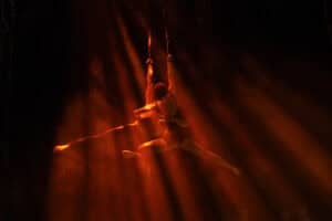 Aerial silk performer in mid-air during a dance routine with dramatic lighting.