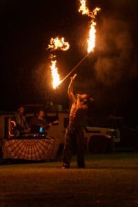 Fire performer creating fire poi at night with a live band in the background.