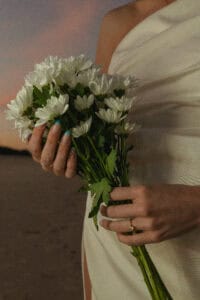 Bride holding a bouquet of white chrysanthemums at sunset.