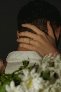 Close-up of a bride and groom embracing, focus on wedding ring and floral bouquet.